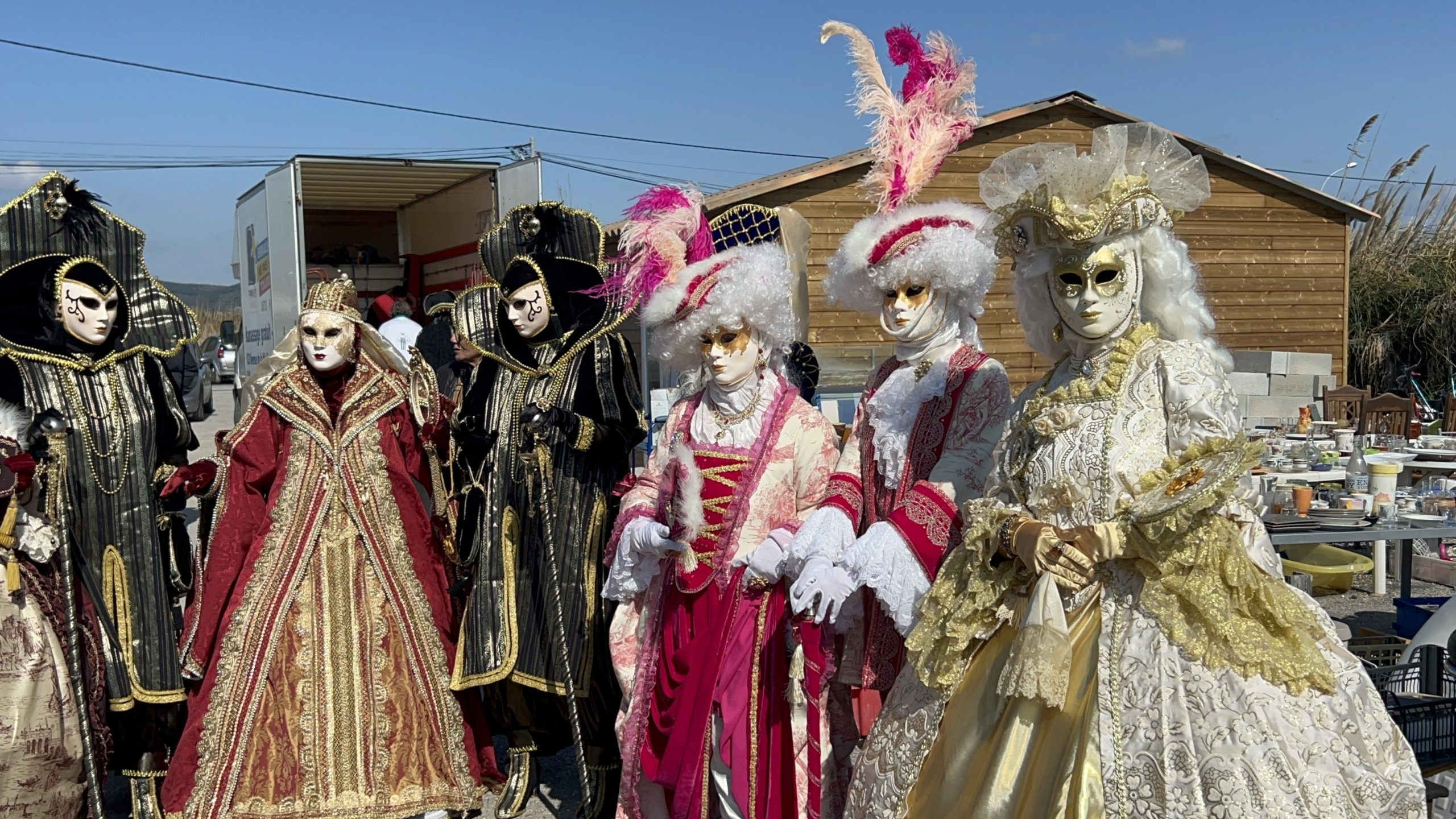 Cinq personnes en costumes vénitiens posent devant les bibelots d'Emmaüs