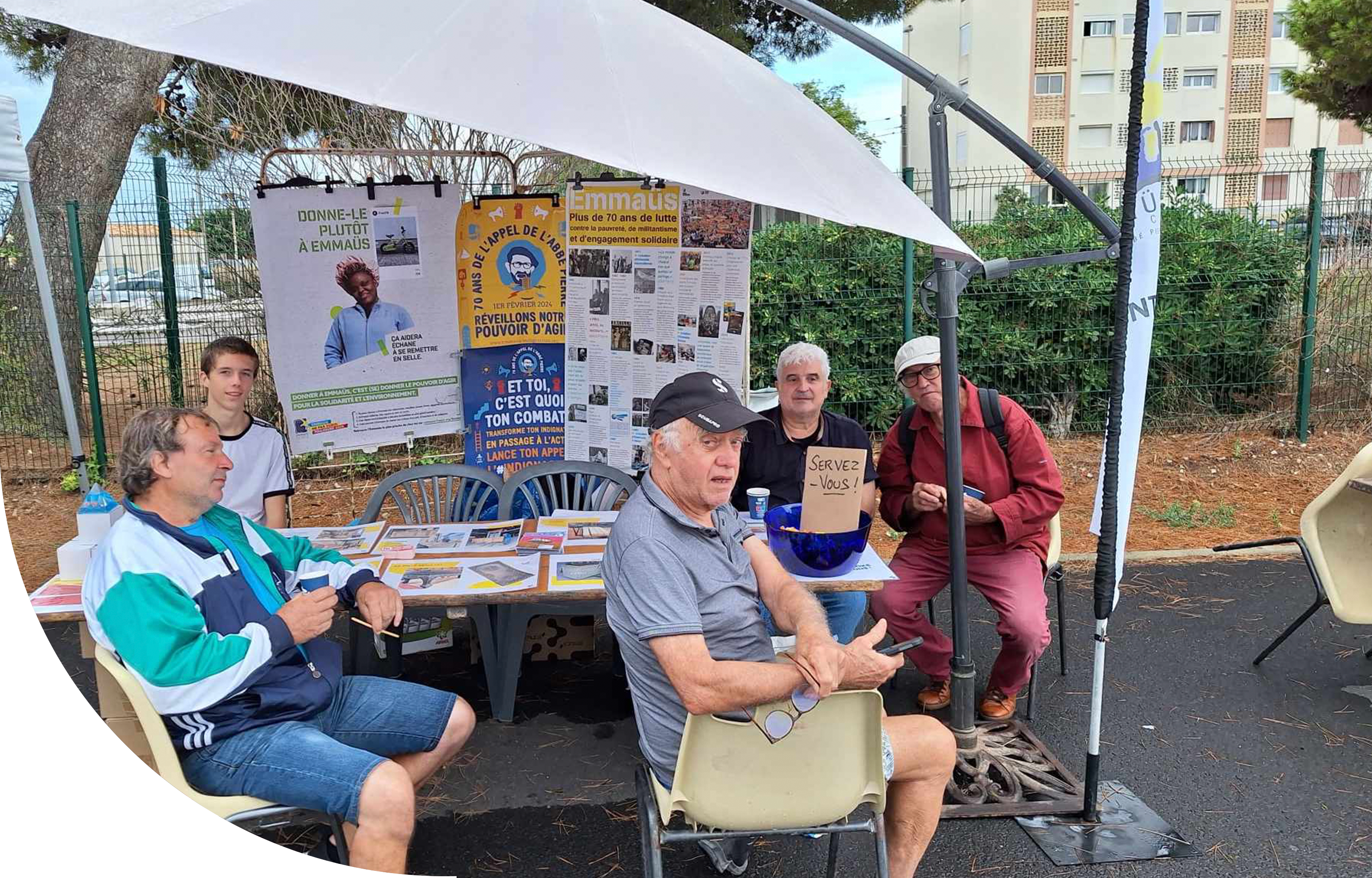 Une table avec cinq hommes assis à l'extérieur lors d'un festival promouvant les vertus d'Emmaüs
